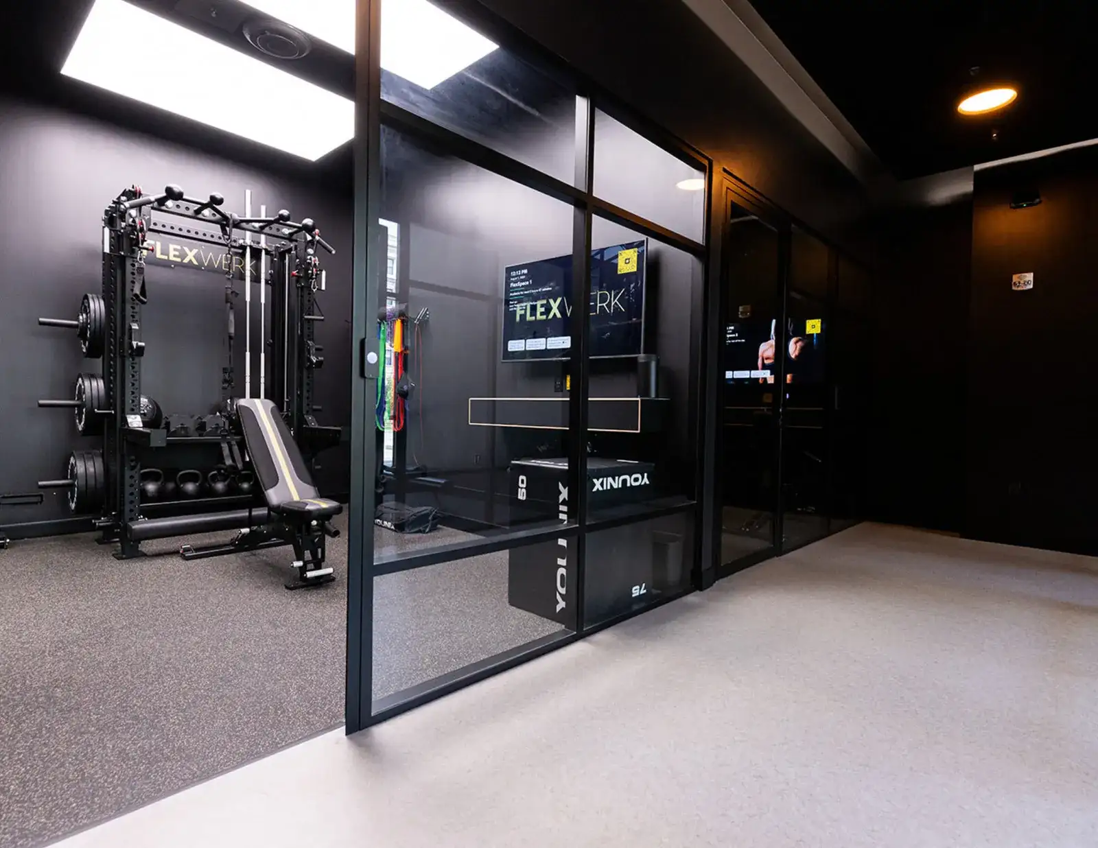 A private FlexWerk suite behind a glass wall, with a rack, bench and wall screen