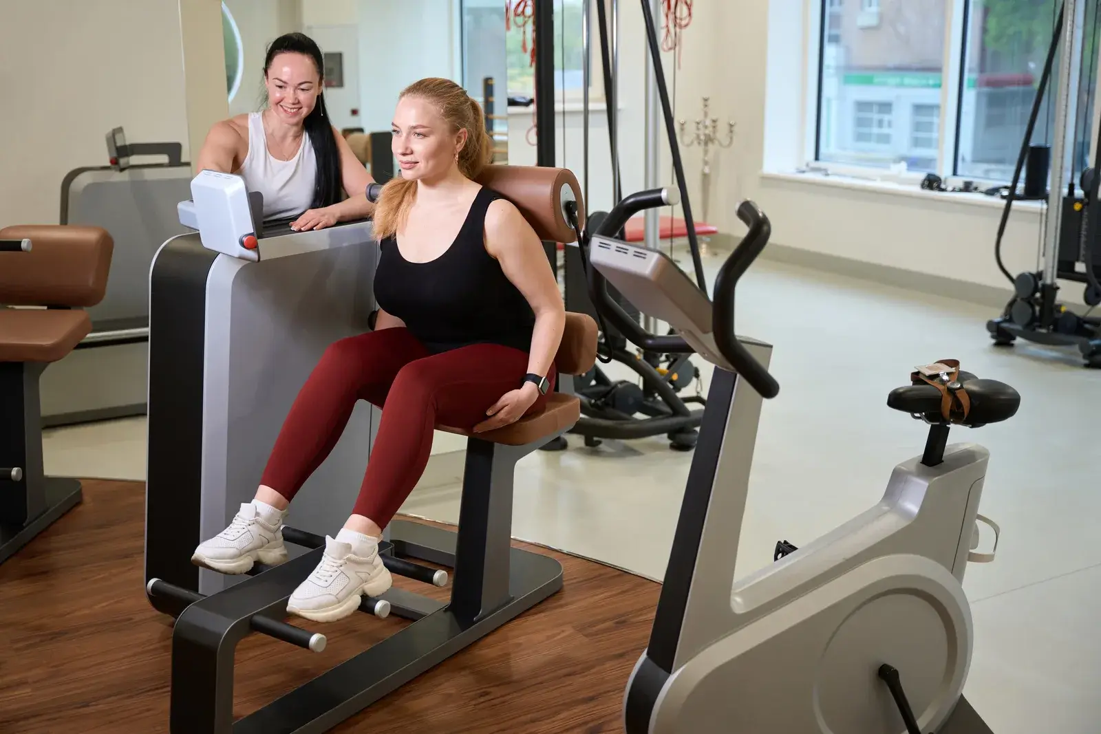 A woman using a seated exercise machine while an instructor checks the machine’s display