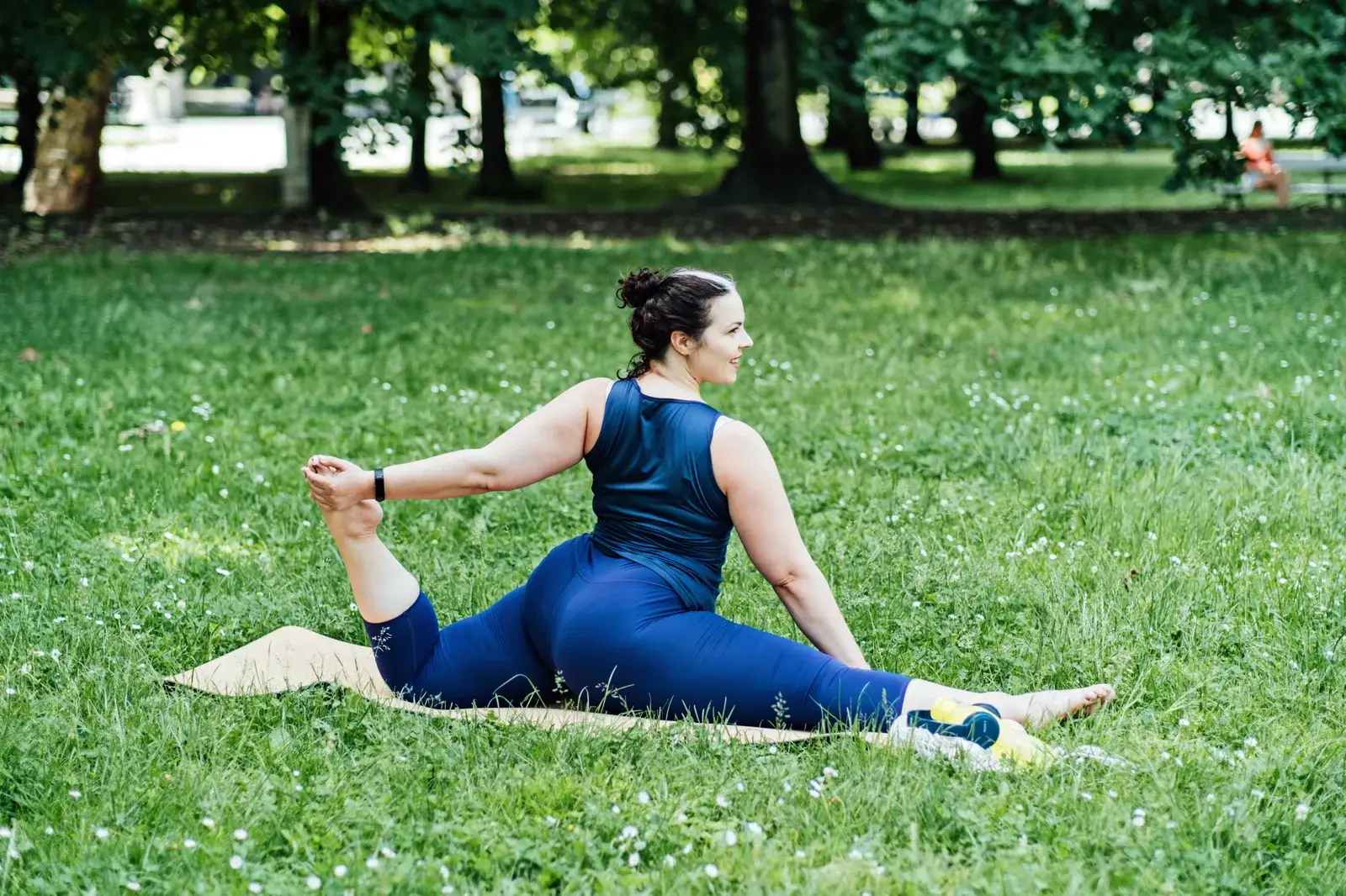 A woman in athletic wear holds a low lunge hip stretch outdoors on a mat