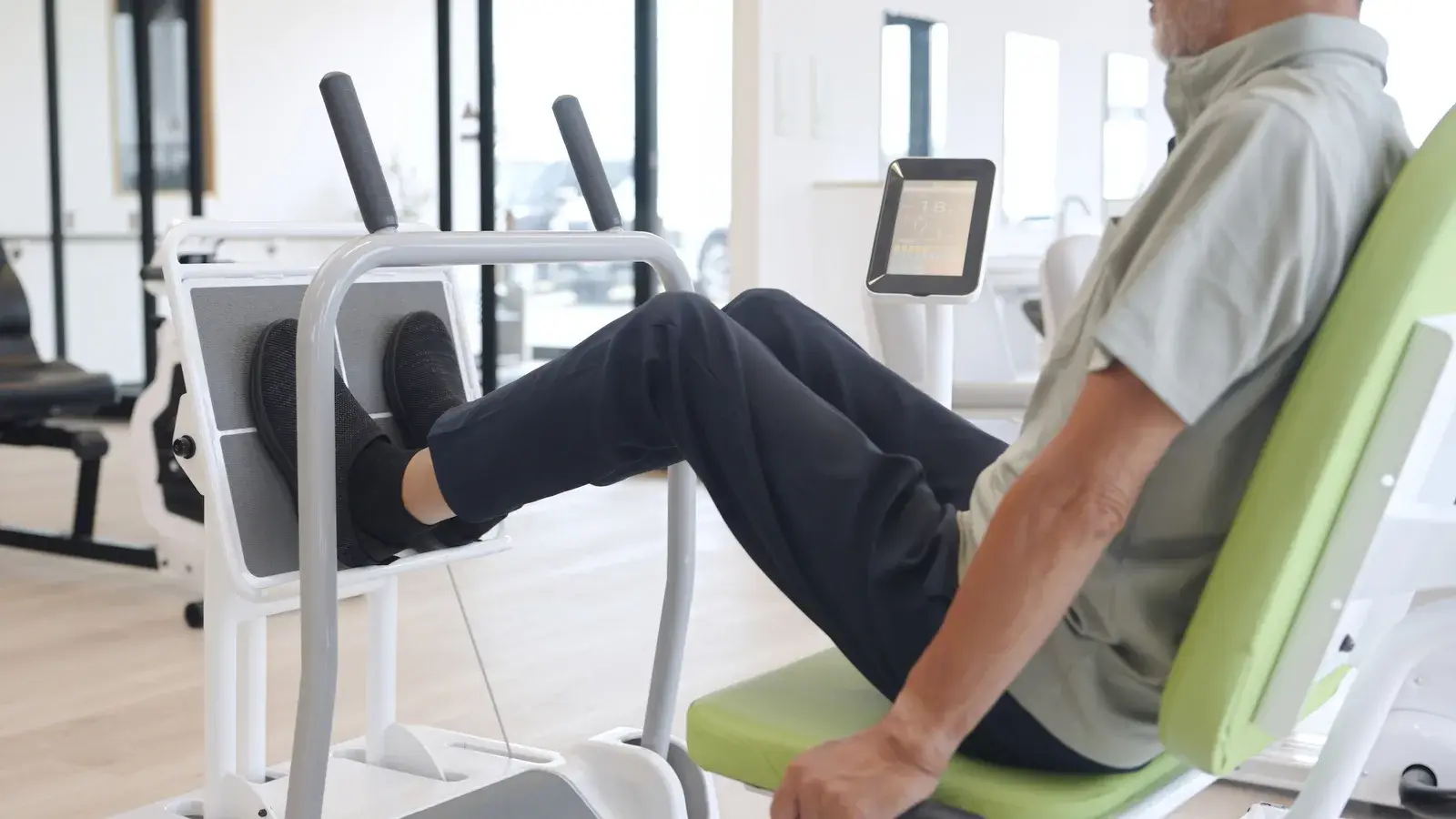 An older adult pushes through a seated leg press machine in a clinic gym