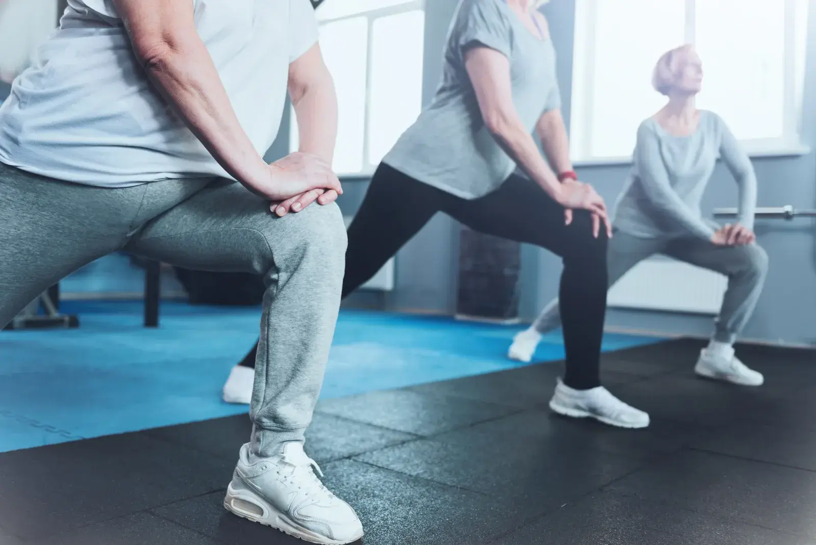Older adults doing side lunges with their hands resting on their knees.